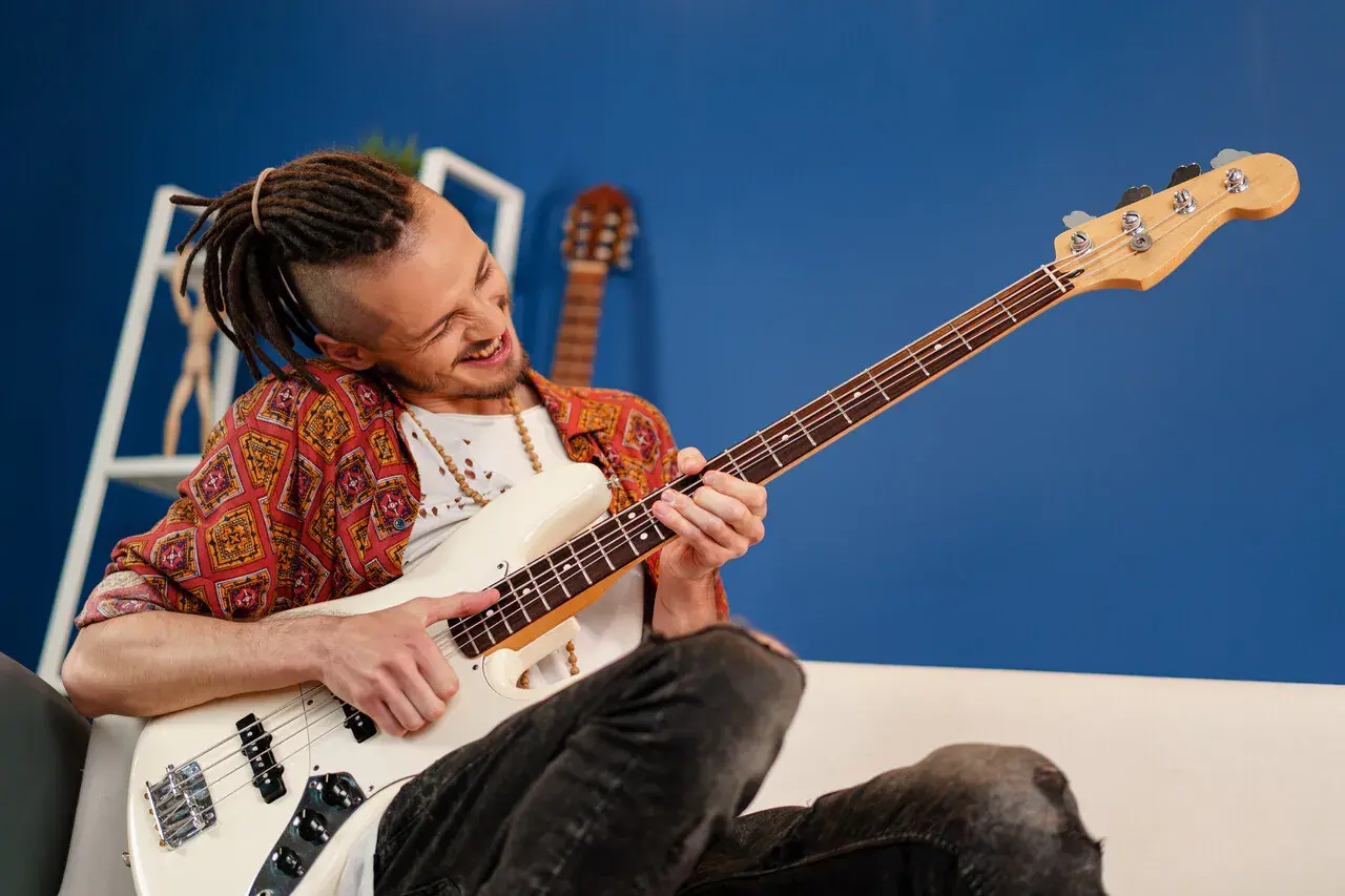 Mężczyzna z dredami gra na białej gitarze basowej typu semi hollow body, z pasją i uśmiechem.