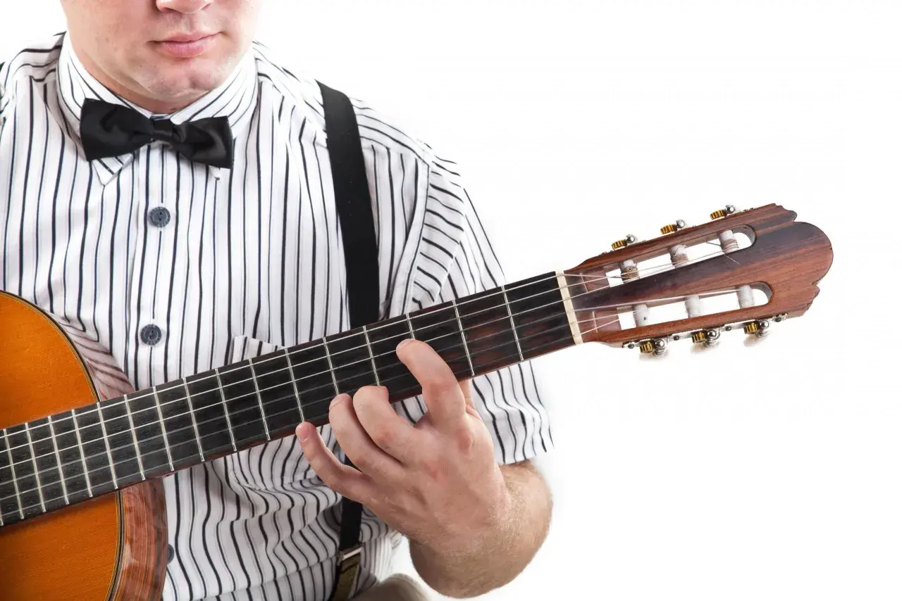 Mężczyzna w koszuli w paski i muszce gra na gitarze. Pokazuje, jak czytać tabulaturę, naciskając struny.