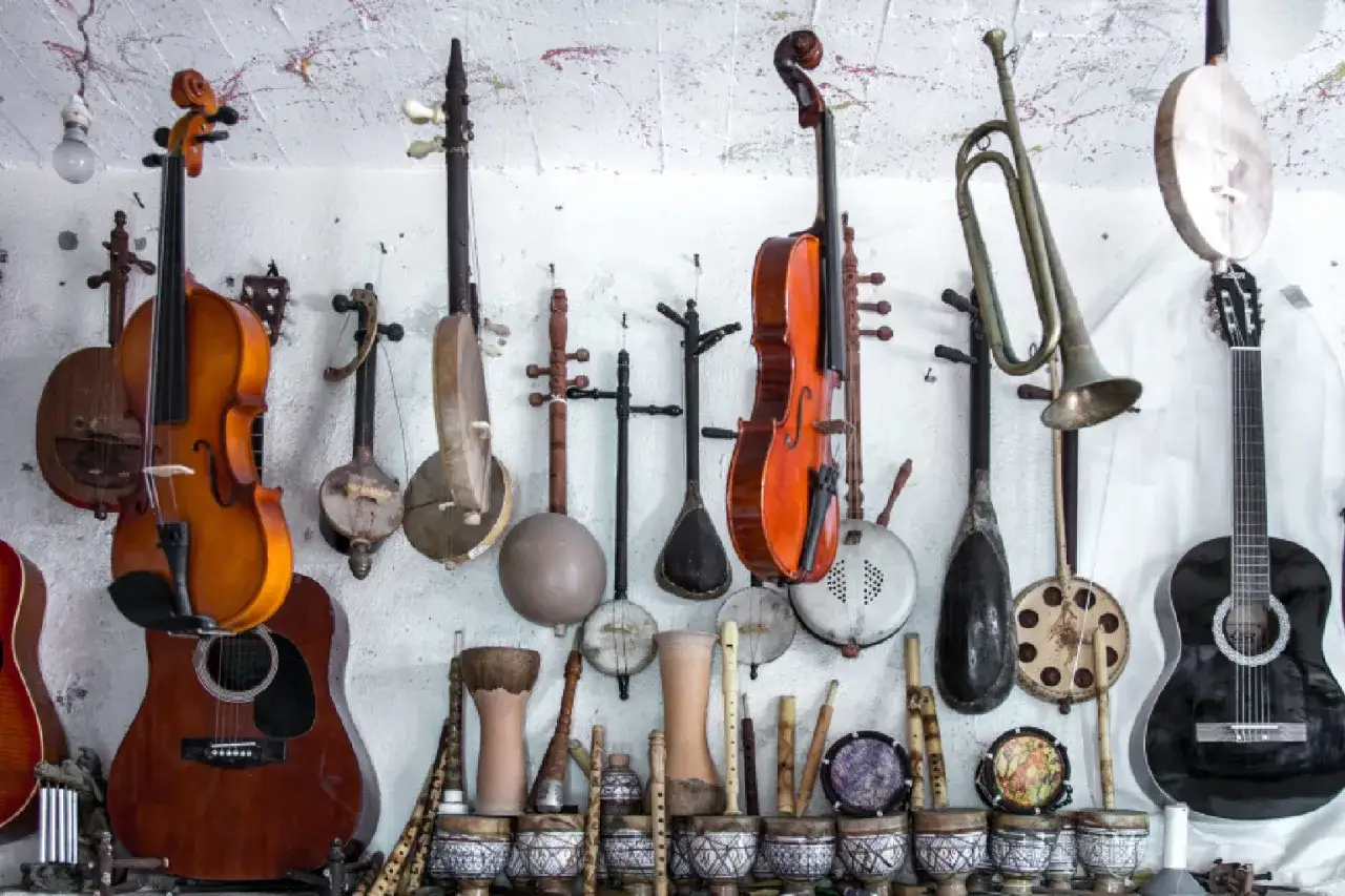 Kolekcja instrumentów strunowych szarpanych: skrzypce, gitary, lutnie i inne, wiszące na ścianie obok instrumentów dętych.