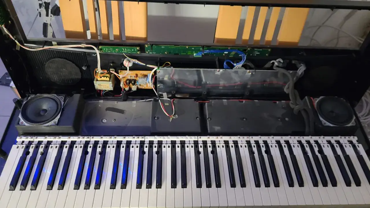 Wnętrze keyboardu podczas naprawy. Widoczne głośniki, płytki drukowane, kable i klawisze.