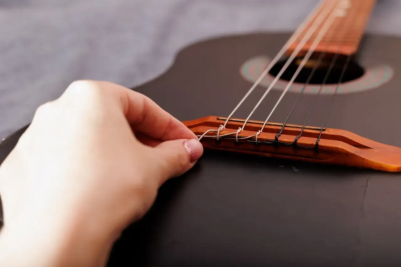 Dłoń mocuje nową strunę podczas wymiany strun w gitarze klasycznej.