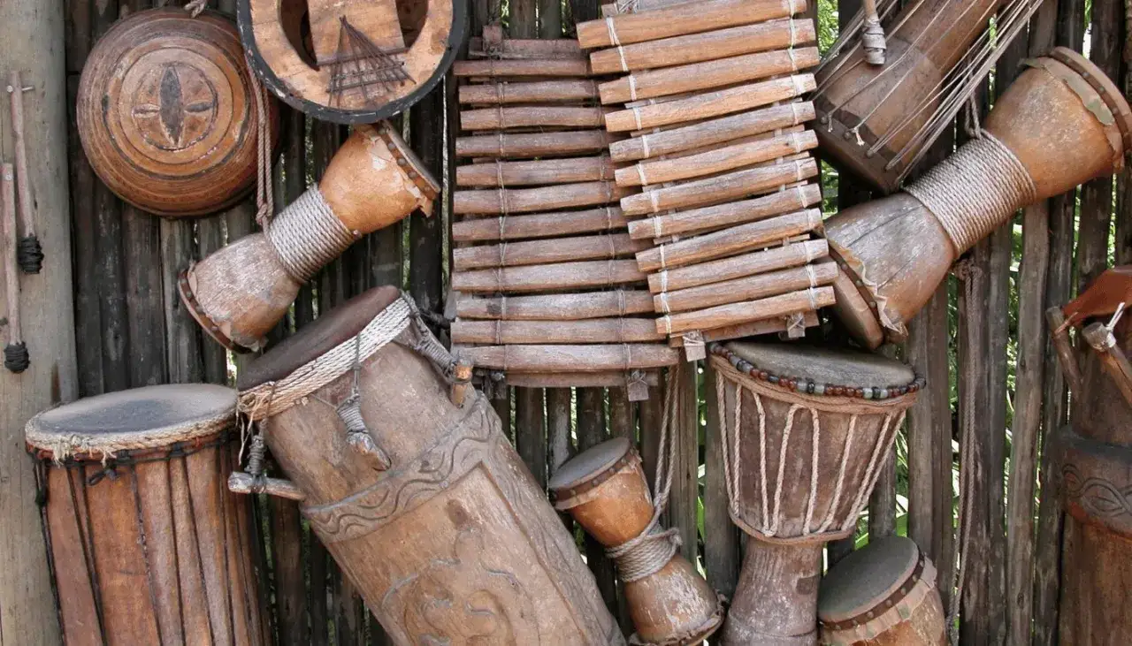 Kolekcja drewnianych bębnów i ksylofonu. Różnorodne instrumenty perkusyjne, niektóre ozdobione sznurkami i rzeźbieniami, tworzą rytmiczną kompozycję.